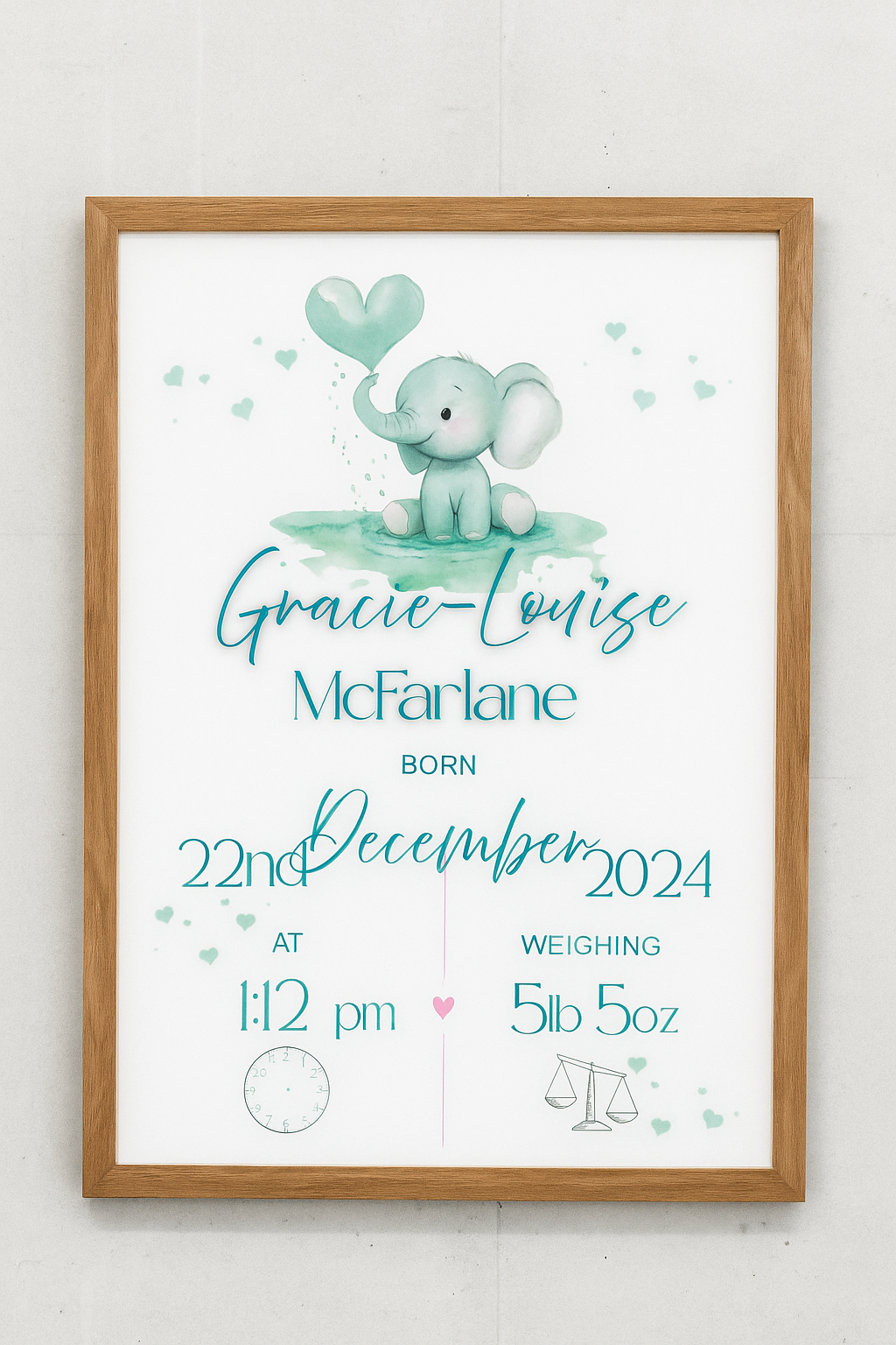 Framed baby poster with elephant illustration and birth details on a white wall.